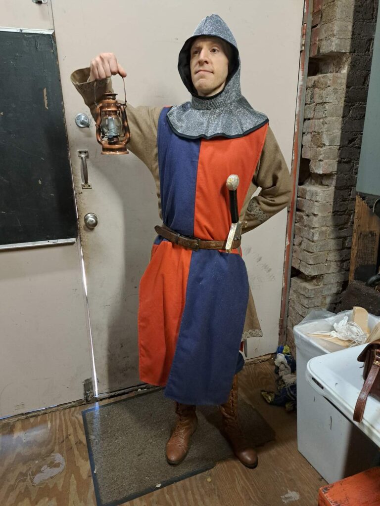 A man in a knight outfit holds a lamp aloft