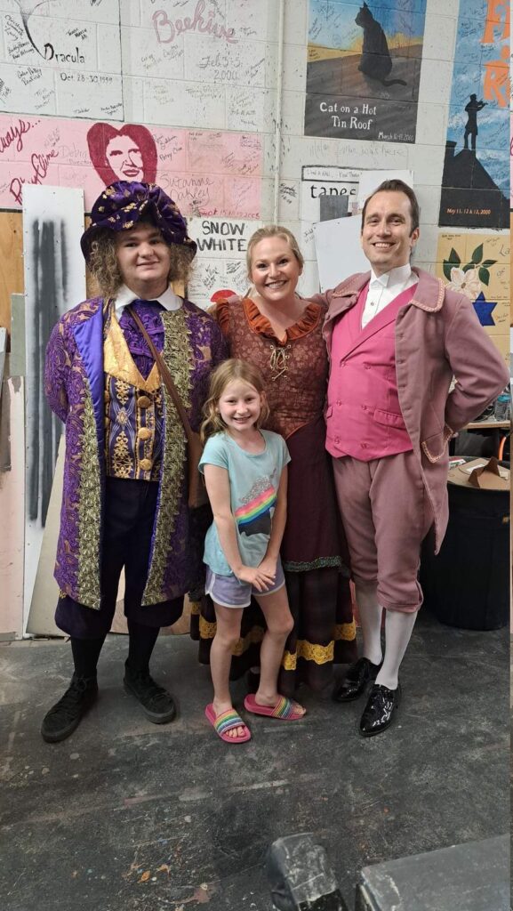 A group of people standing backstage, smiling at the camera