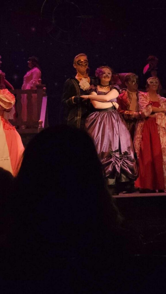 A man holding a woman in fancy dress and mask, during a dance