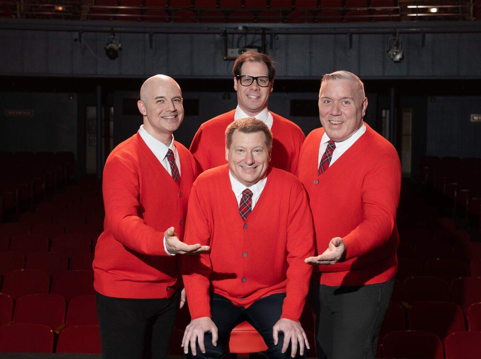 Four men in matching red cardigans and plaid ties smiling onstage for a Plaid Tidings promotional photo.